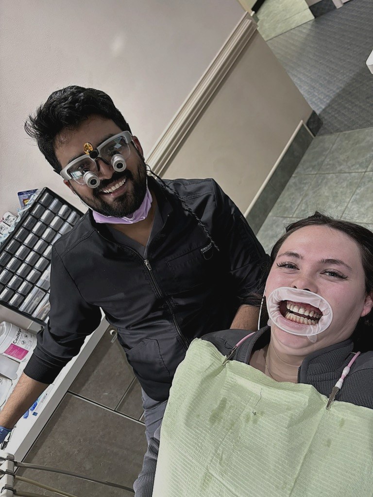 Dr. Nishant in goofy googly-eye dental loupes, laughing with a happy patient in the chair.