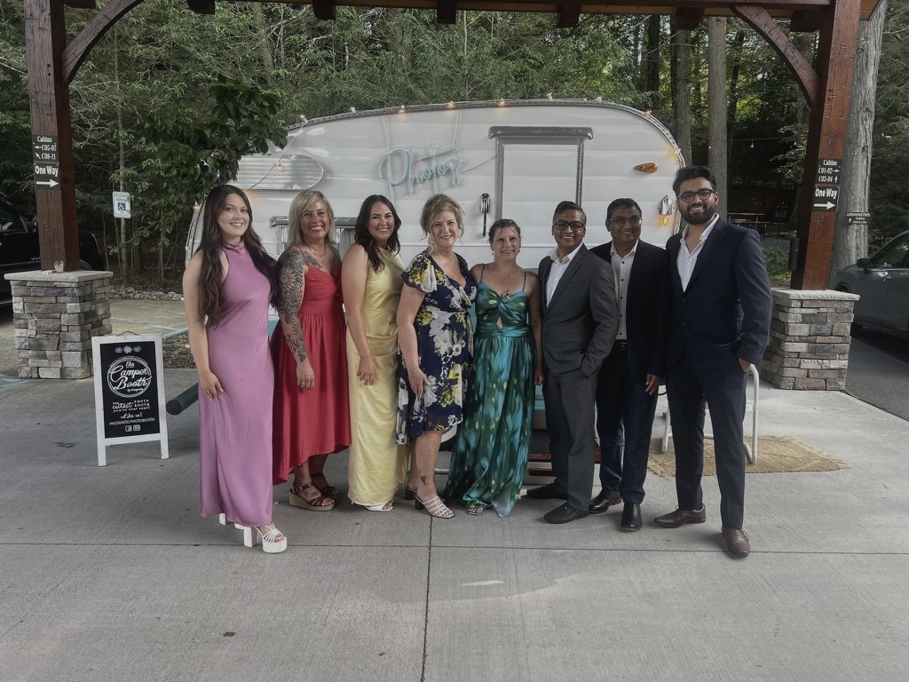 The team dressed up at a formal wedding, posing in front of a vintage camper photo booth.